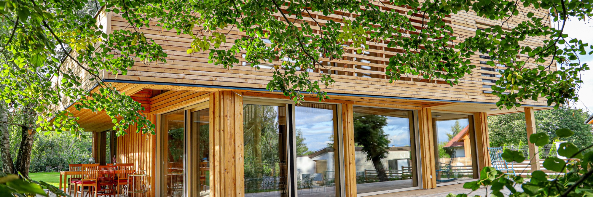 Ein zweistöckiges Wohnhaus aus Holz mit vielen Glastüren und Fenstern im Grünen