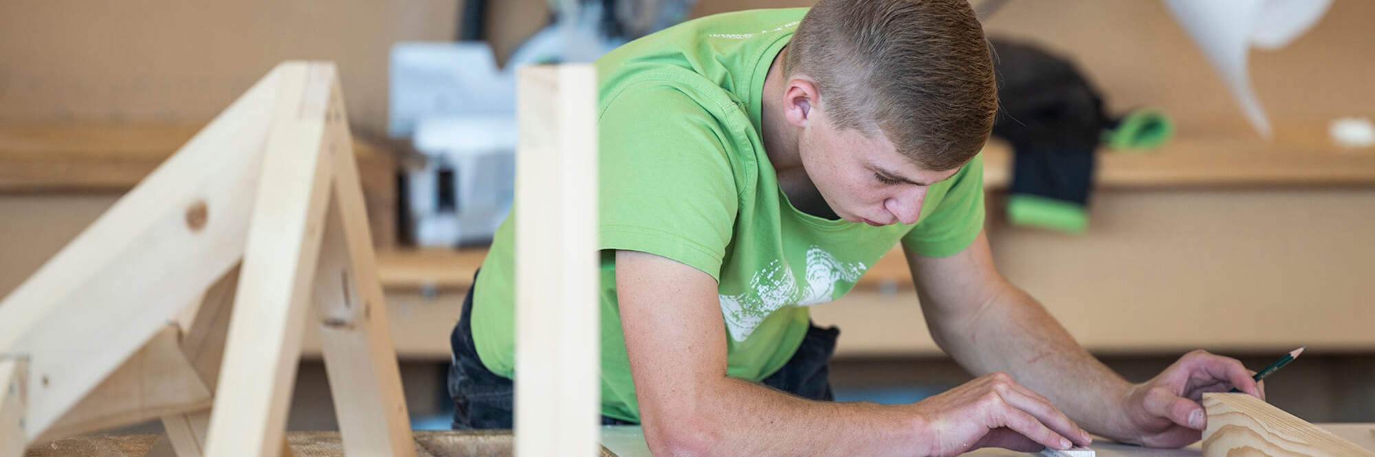Ein junger Holzbau-Meister-Lehrling misst ein Holzstück ab
