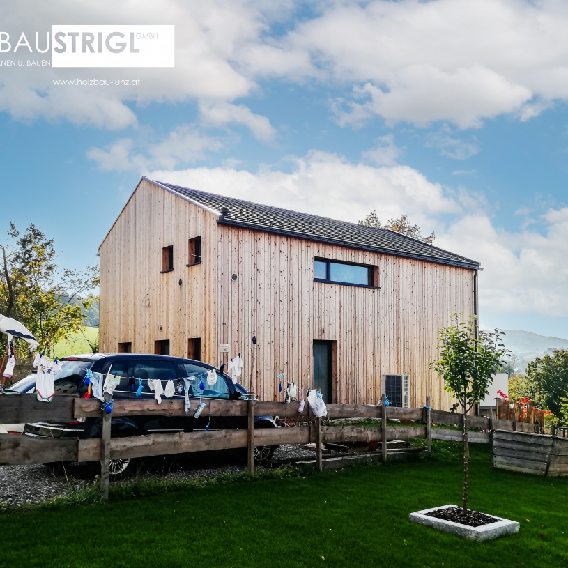 Ein zweistöckiges Wohnhaus aus ausgeblichenem Holz mit vielen Pflanzen im Garten