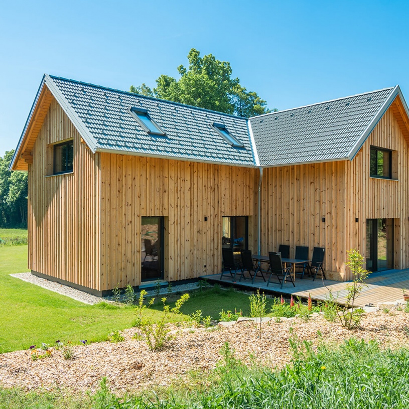 Ein zweistöckiges Wohnhaus aus hellem Holz mit kleinen Fenstern und einem Garten rundherum