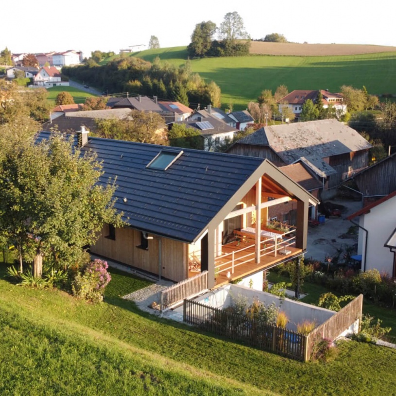 Ein Hanghaus mit großer Holzterrasse wird von der Sonne bestrahlt