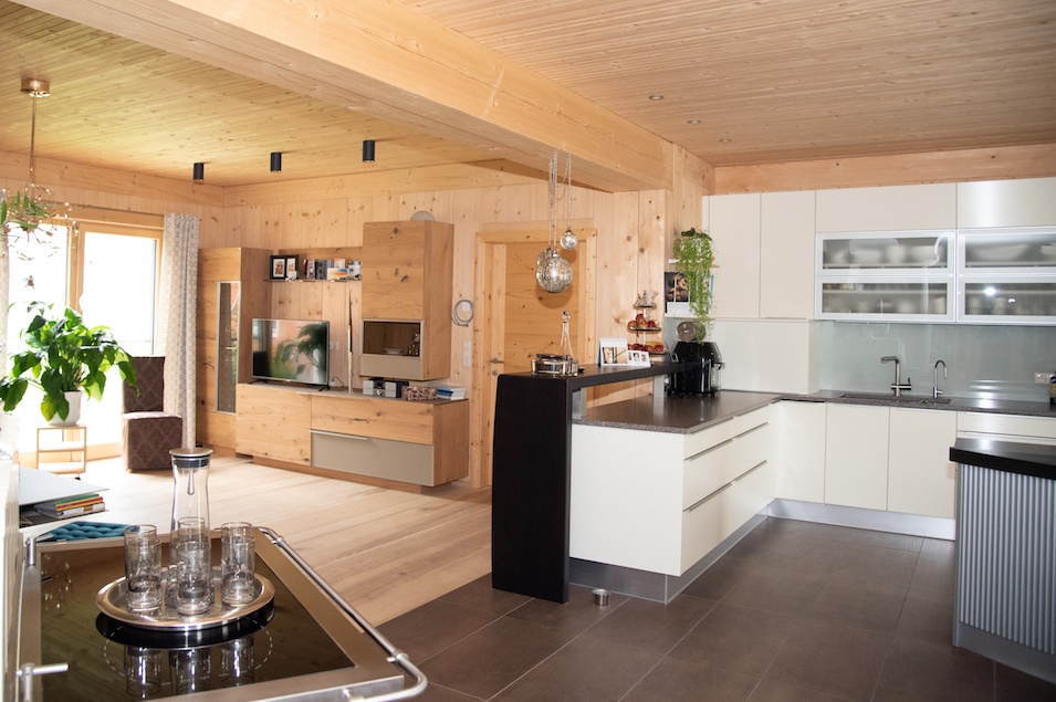 Geräumiger Wohn- und Essbereich mit weißer Küche und großem Holzzubau links