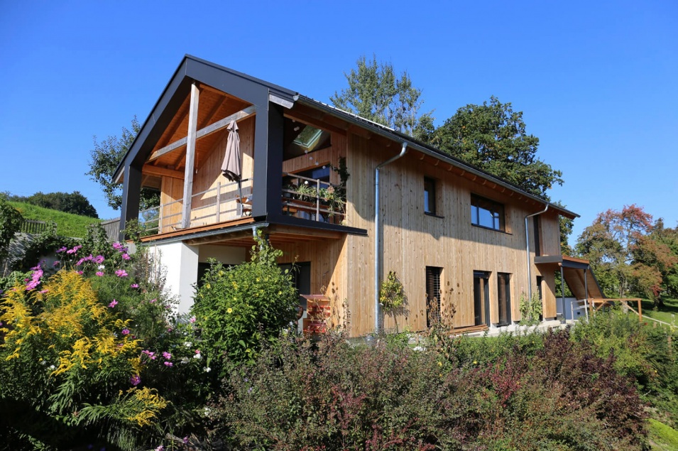 Mit Holz verkleidetes Haus mit großem Balkon vor vielen Pflanzen