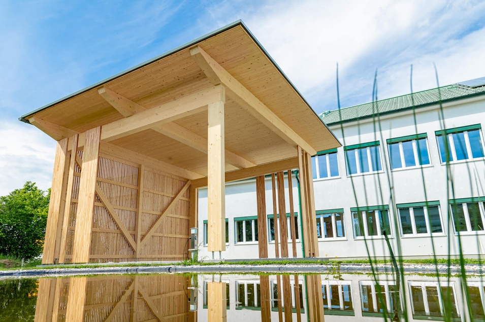 Überdachte Räumlichkeit aus Holz neben weißem Gebäude mit Spiegelung in Wasser