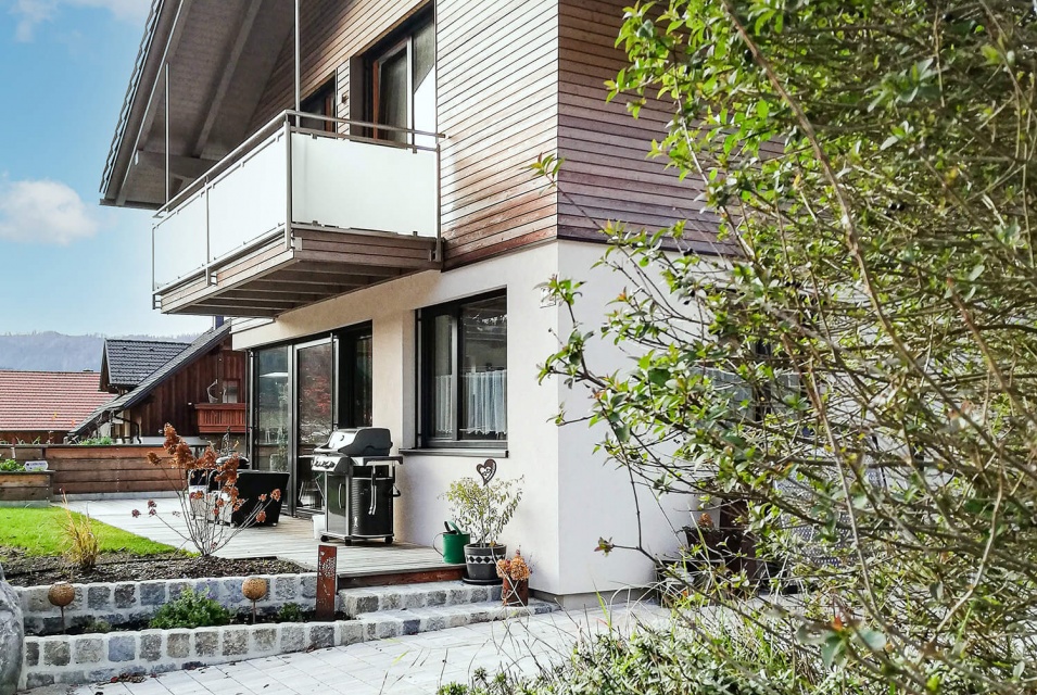 Ein weißes Haus mit Satteldach, Holzverkleidung und einem Balkon im ersten Stock.