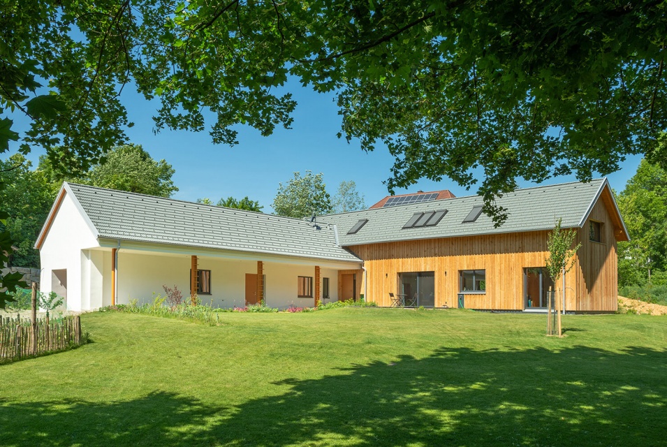 Ein weißes Haus und ein Holzhaus sind miteinander verbunden und teilen sich einen großen Garten