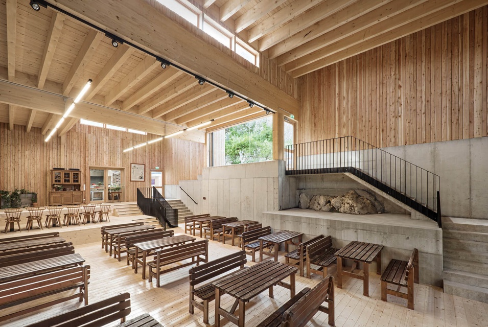 Geräumiger Innenbereich einer Holzhalle mit zahlreichen Holztischen und Bänken