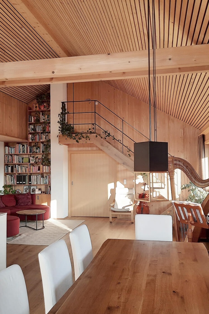 Geräumiger Wohn- und Essbereich aus Holz mit rotem Sofa links und einer großen Harfe rechts