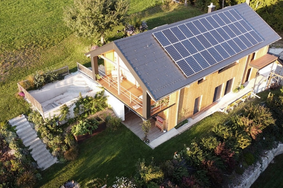 Vogelperspektive eines großen Holzhauses inkl. großem Balkon und Solar-Panels auf dunkelgrauem Dach