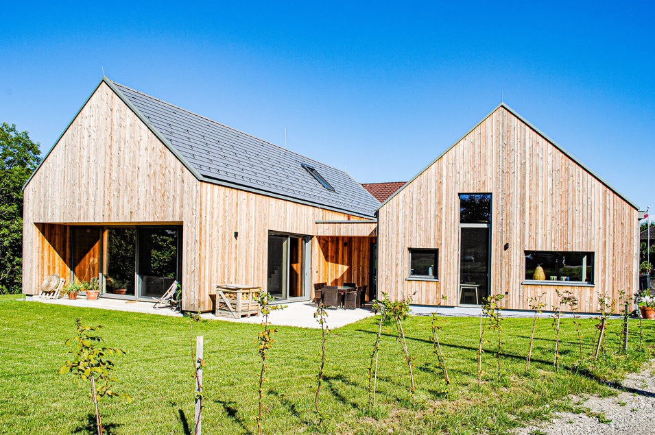 Zwei Wohnhäuser aus Holz stehen nebeneinander und haben einen gemeinsamen Garten mit kleinen Bäumen am Rand