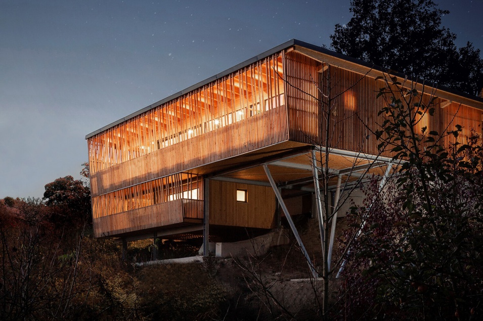 Ein stark beleuchtetes Holzhaus auf Stahlstützenin einem Wald