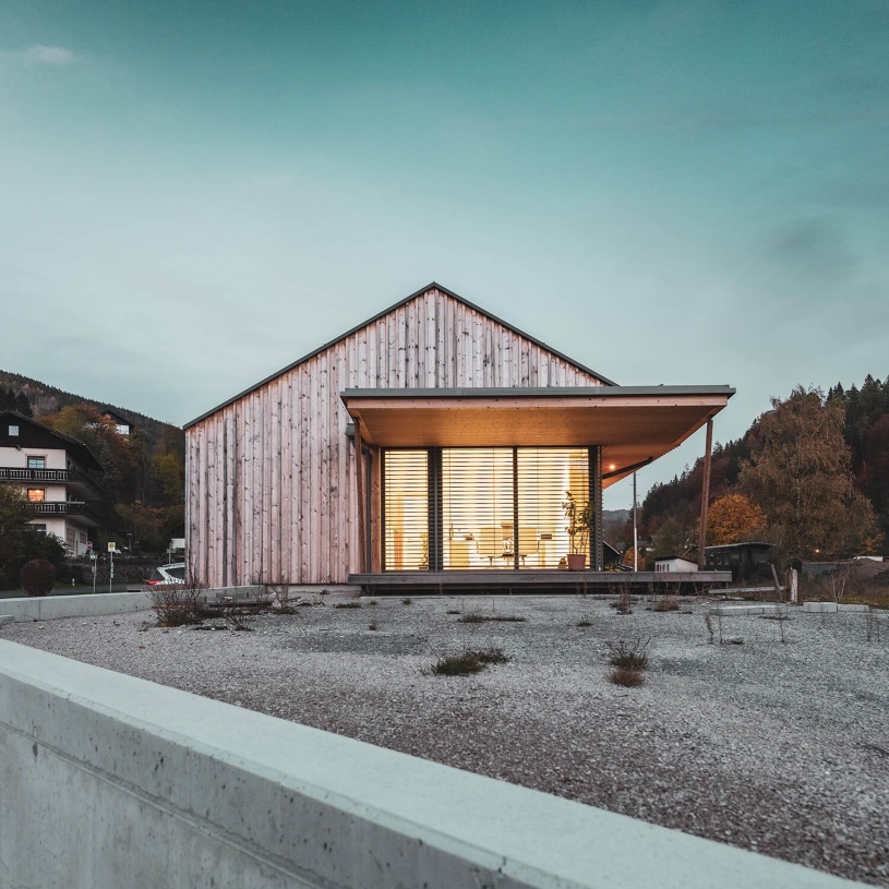 Frontale Ansicht eines Holzhauses mit großer Terrasse und beleuchtetem Innenraum