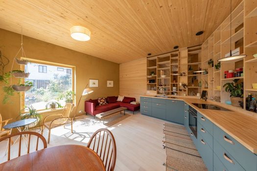 Innenansicht eines geräumigen Wohn- und Essbereichs vollkommen aus Holz mit blauen Küchenmöbeln und Schränken