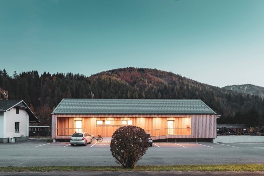 Holzhaus mit beleuchtetem Außenbereich und geparktem Auto davor mit imposantem Hügelpanorama dahinter