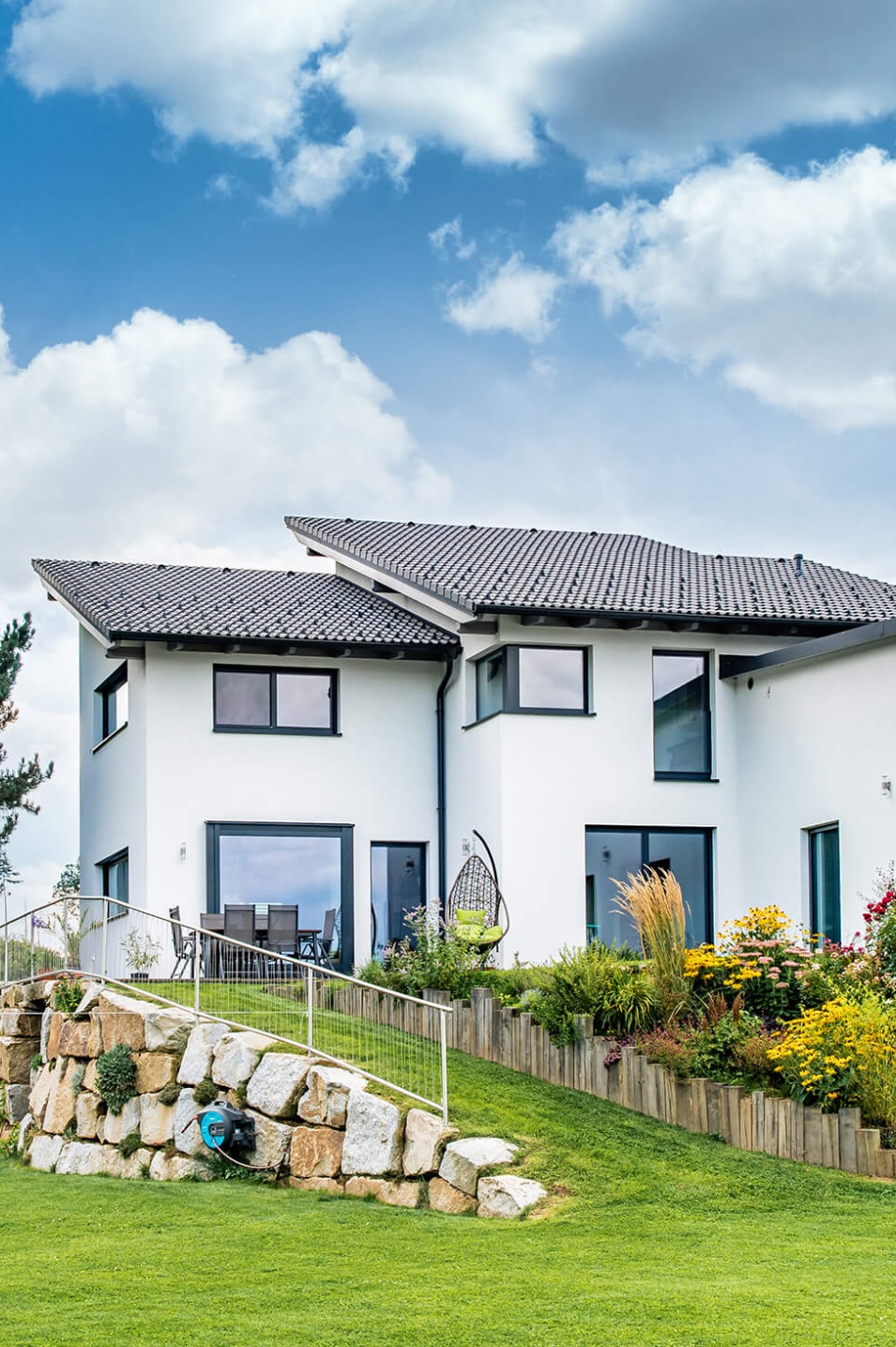 Rückseite eines weißen Hauses mit großem Garten und Steinmauer davor.