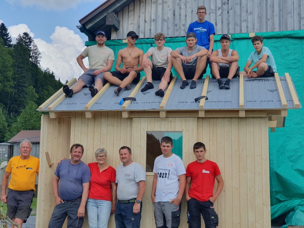 Menschen stehen vor und sitzen auf dem Dach, einer kleinen Holzhütte.