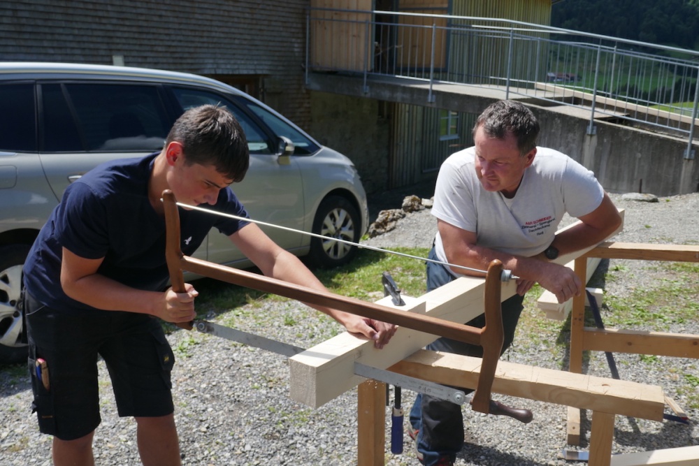 Junger Zimmerer sägt Holz und der Betreuer schaut zu.